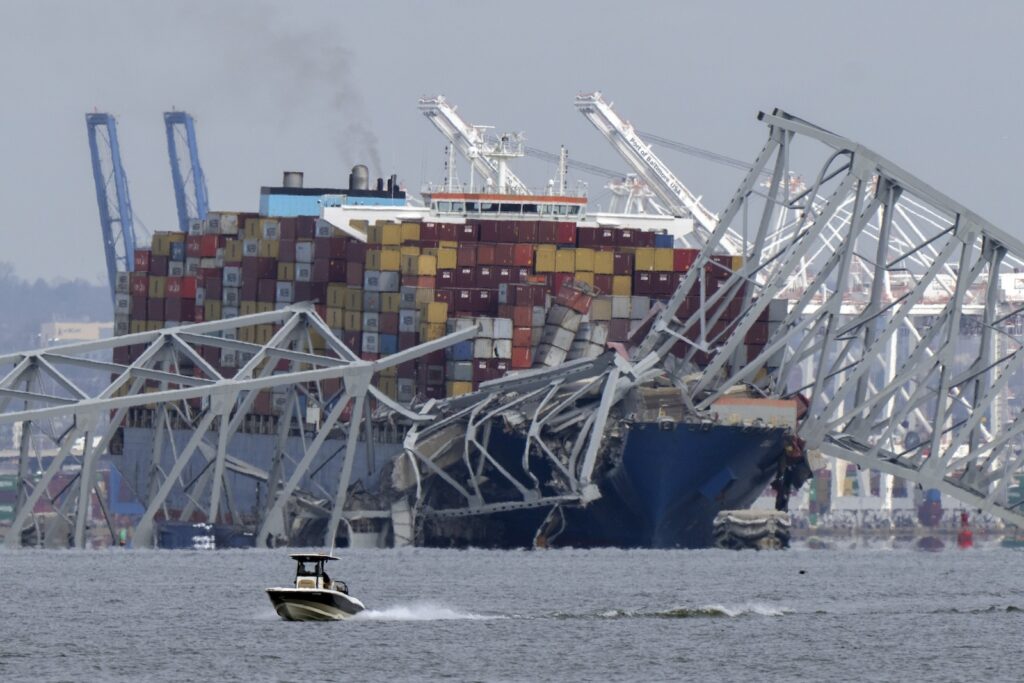 A boat moves past a container ship as it rests against wreckage of the Francis Scott Key Bridge on Tuesday, March 26, 2024, as seen from Pasadena, Md