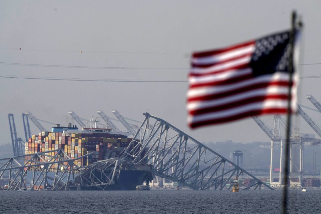 An American flag flies on a moored boat as the container ship Dali rests against wreckage of the Francis Scott Key Bridge, Tuesday, March 26, 2024, as seen from Pasadena, Md.