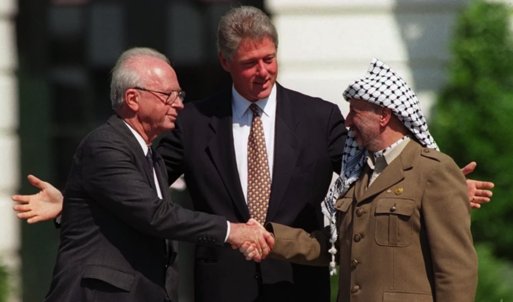 clinton-rabin-arafat-ap-2024-03-13 Bill Clinton looks on as Yitzhak Rabin and Yasser Arafat shake hands