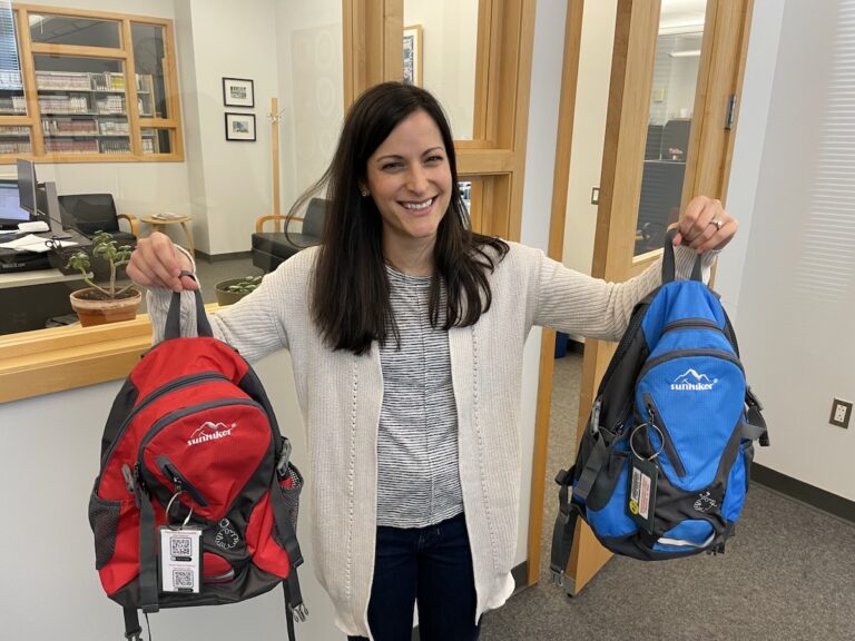 Erica Bess holds up two backpacks, smiling