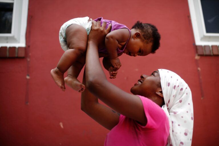 A mother holds her daughter in the air.