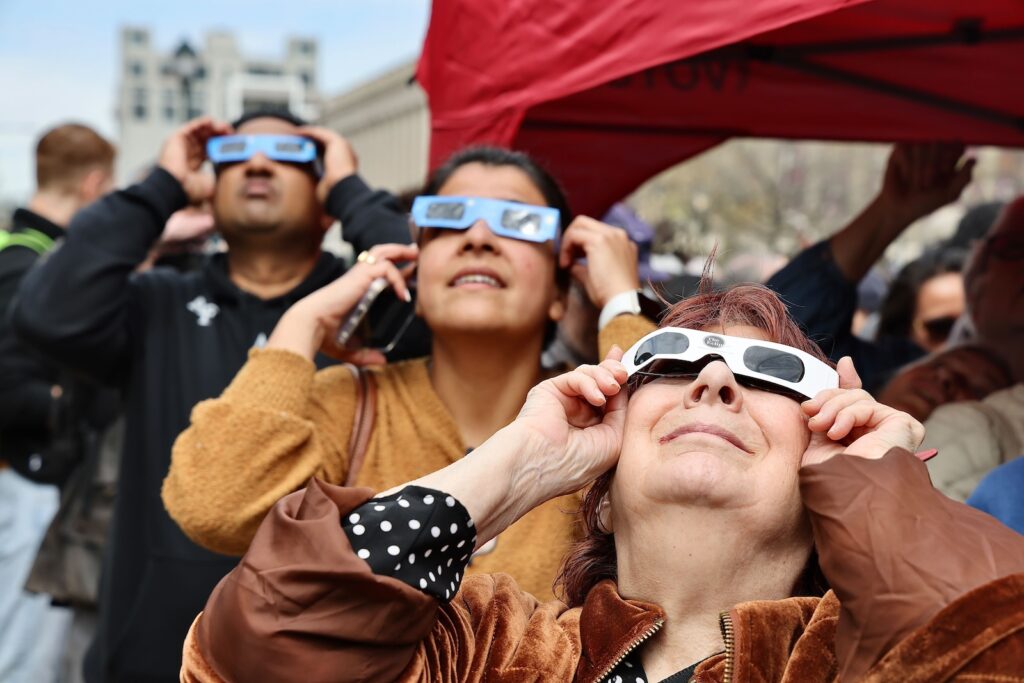 solar-eclipse-philadelphia-franklin-institute-01-EL-040824 Three people are seen holding up eclipse glasses as the eclipse streaks across Philadelphia