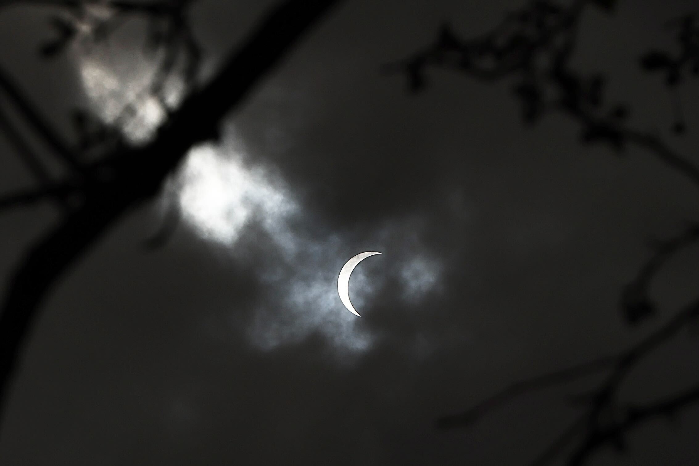 A sliver of sun is visible through a screen of clouds to viewers watching the solar eclipse outside the Franklin Institute in Center City Philadelphia.