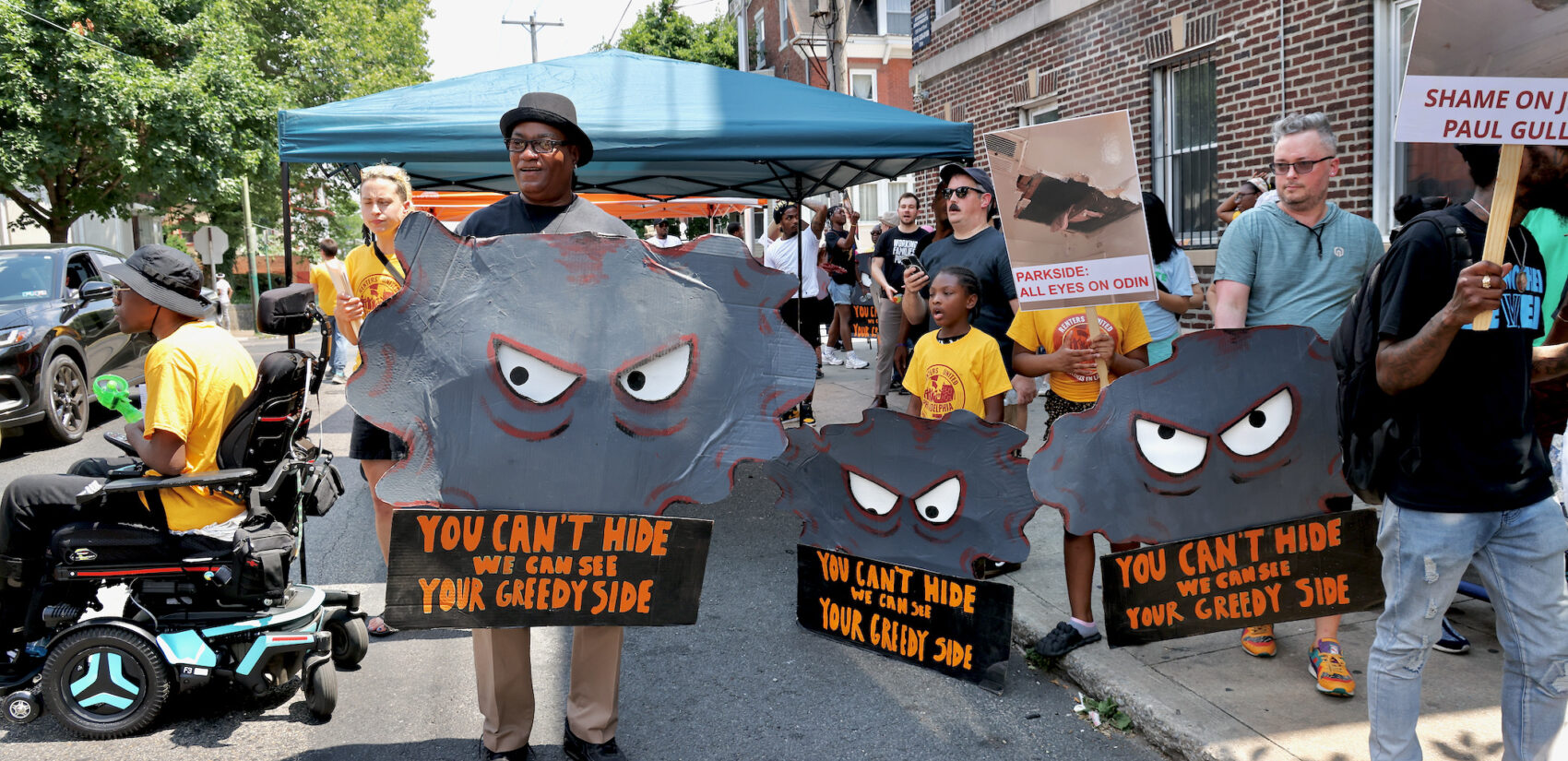 Protesters carry signs reading You Can't Hide We Can See Your Greedy Side