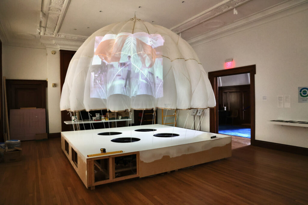 a piece in the Community of Images exhibit shows a jellyfish-like parachute tethered to a square stage