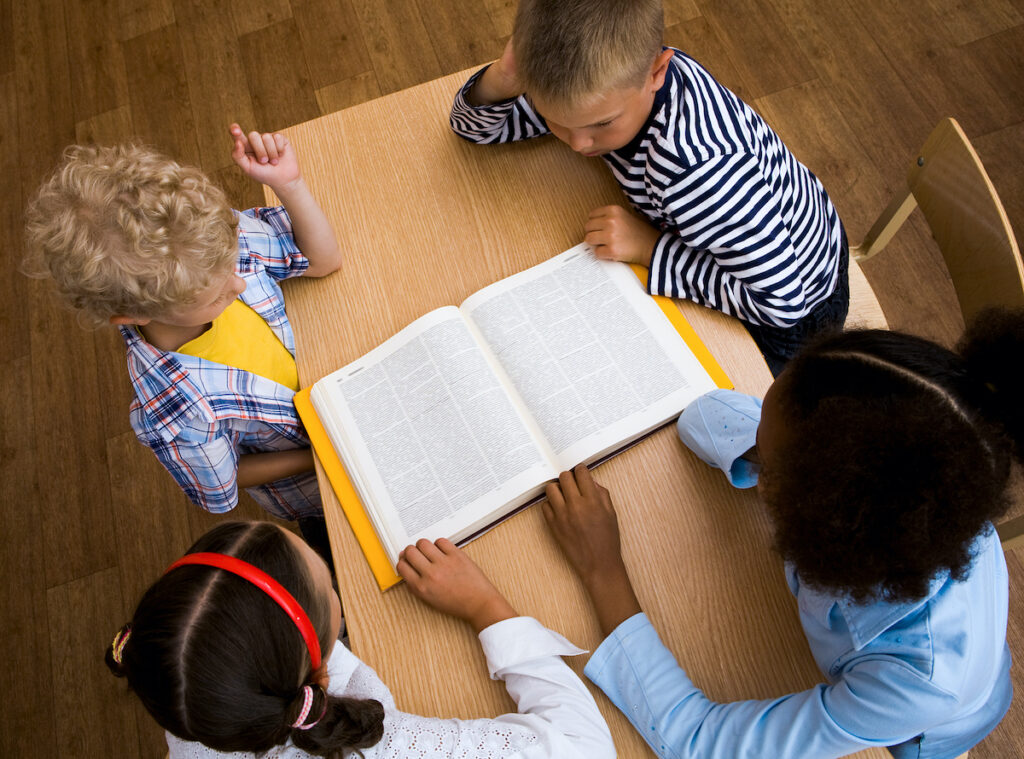 Reading Above view of pupils looking at page of encyclopaedia at reading lesson