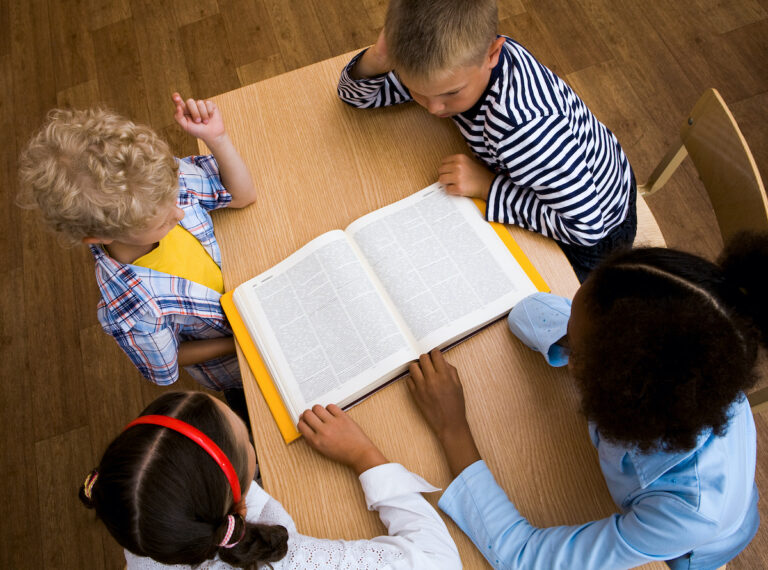 Above view of pupils looking at page of encyclopaedia at reading lesson