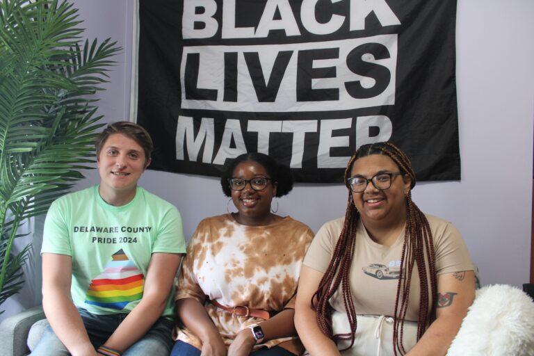 Kyle McIntyre, Dyamond Gibbs and Kayla Cocci are seen sitting on a couch under a Black Lives Matter banner