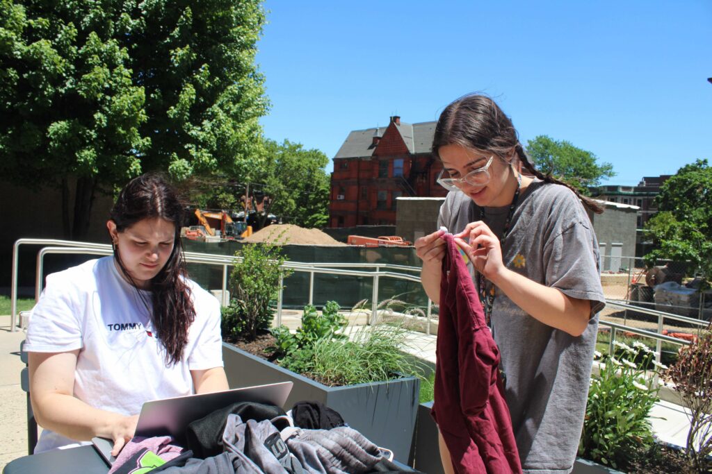 Addie Schenkel, left, a recent Drexel graduate, and Arianna Papadakis, right, a rising junior, work together to collect data on clothing discarded by students during move out. (Emily Neil/WHYY)