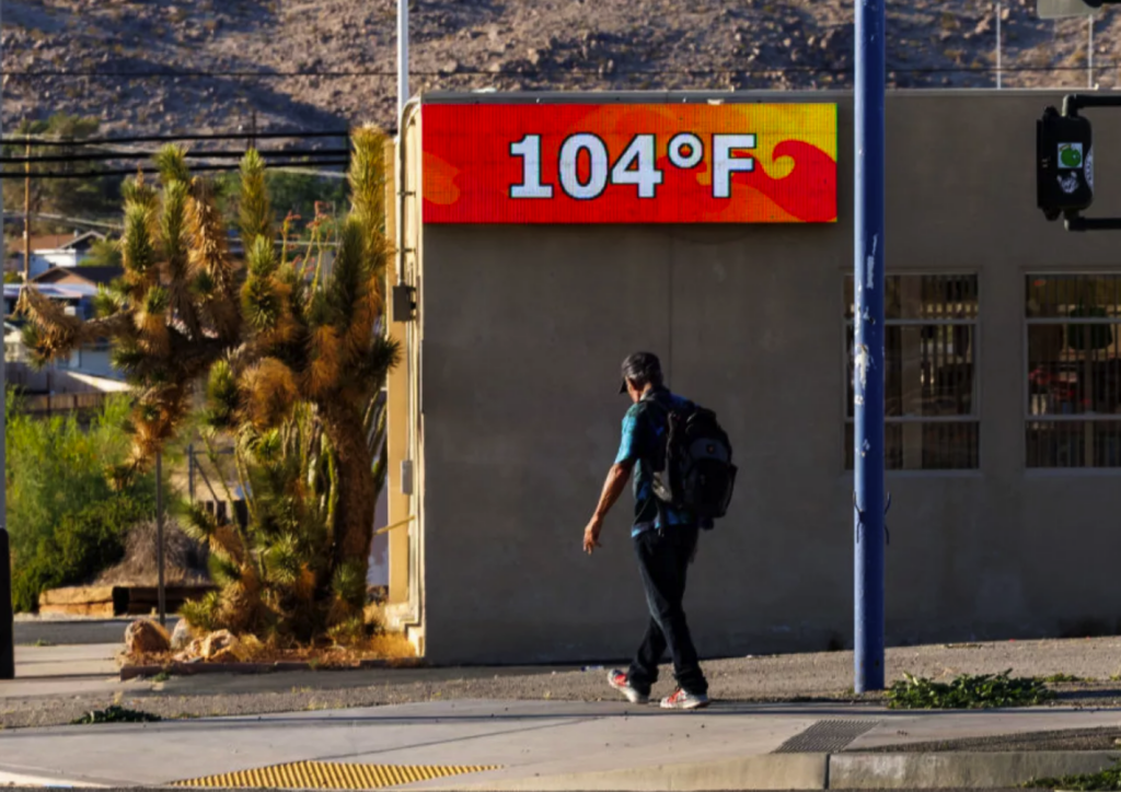 heat-california-npr-getty-2024-06-07 A man walking outside with a digital sign showing temperature is 104 degrees