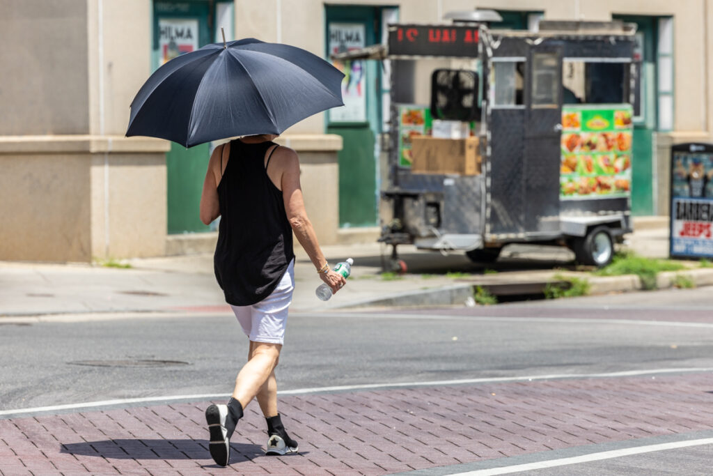 A person walkng down the street with an umbrella to get out of the sun
