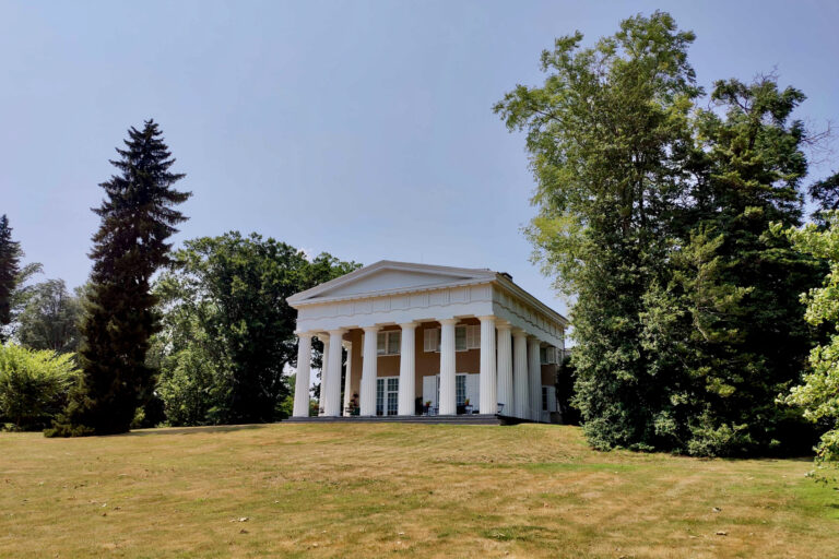 A Grecian columned porch sits between several trees