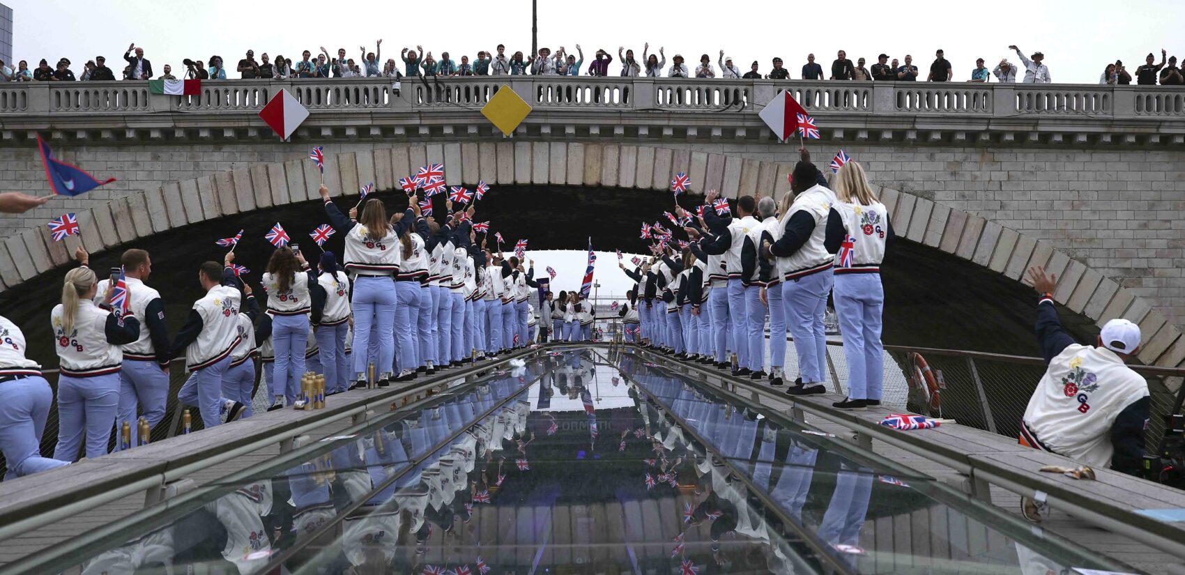 Spectators cheer as Great Britain athletes pass under a bridge along the Seine River during the opening ceremony for the 2024 Summer Olympics in Paris, France, Friday, July 26, 2024. (Naomi Baker/Pool Photo via AP)