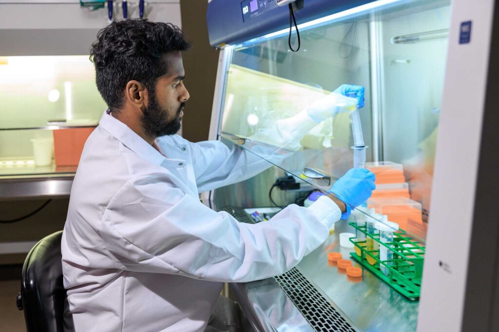 A medical researcher looks at tubes behind plexiglass