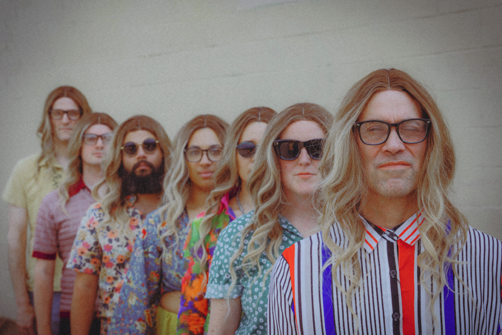 many people standing in a row wearing blond wigs