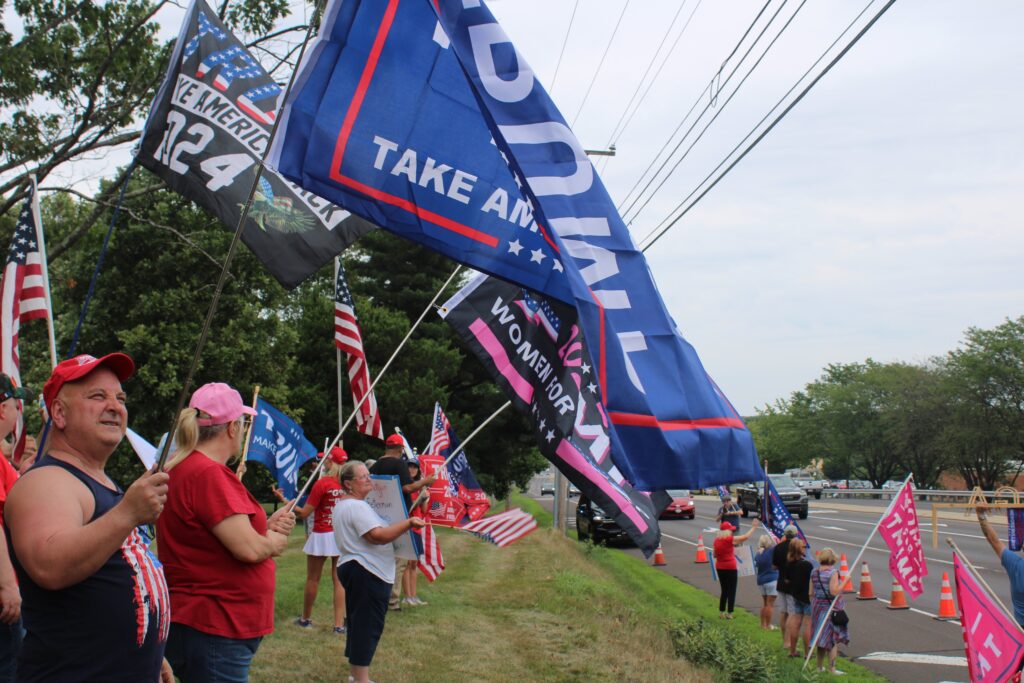 Trump-rally-6 People stand in the grass on the side of the road holding flags supporting Donald Trump for president