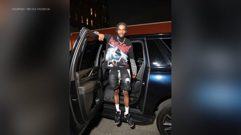 Rapper YBC Dul stands in front of a SUV with its door open