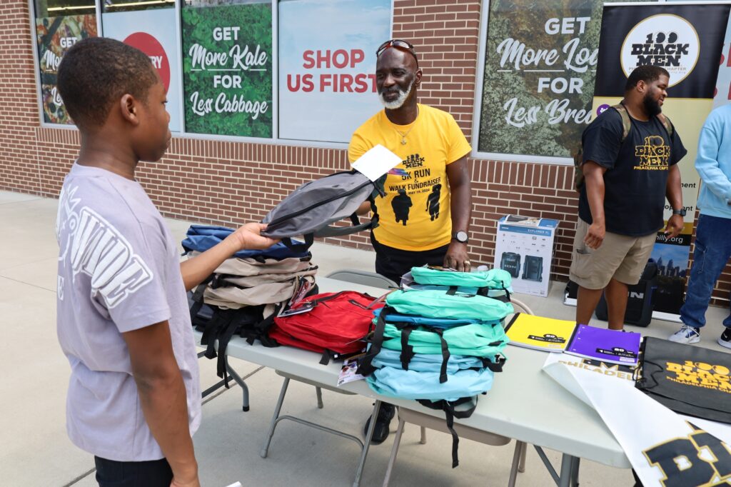 100_black_men_bookbag_school_supplies_giveaway David Chaney, Sr. hands a backpack to a child at a giveaway