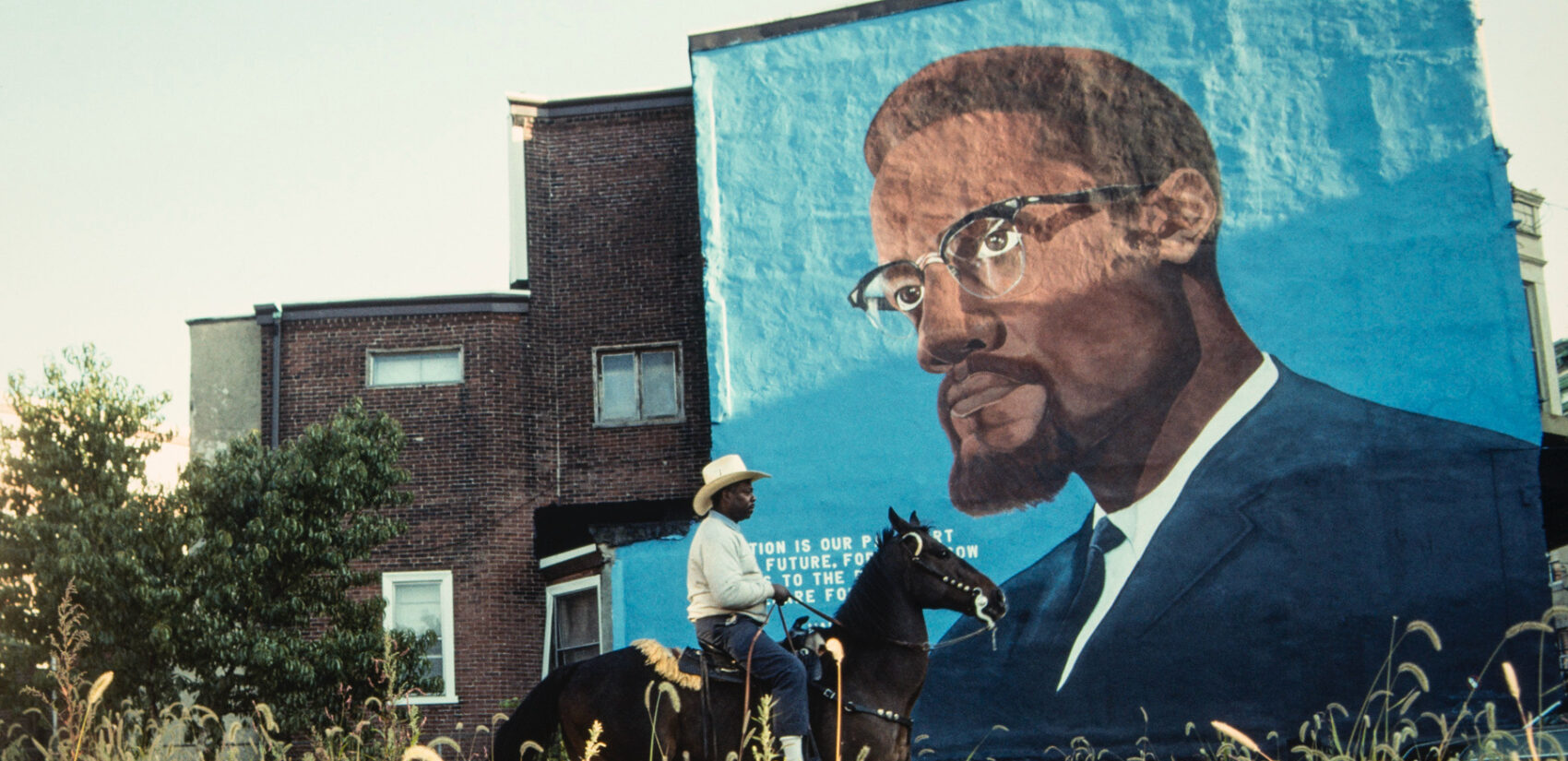 A Black horse rider passes a mural of Malcolm X on a building in Philadelphia in 1993.