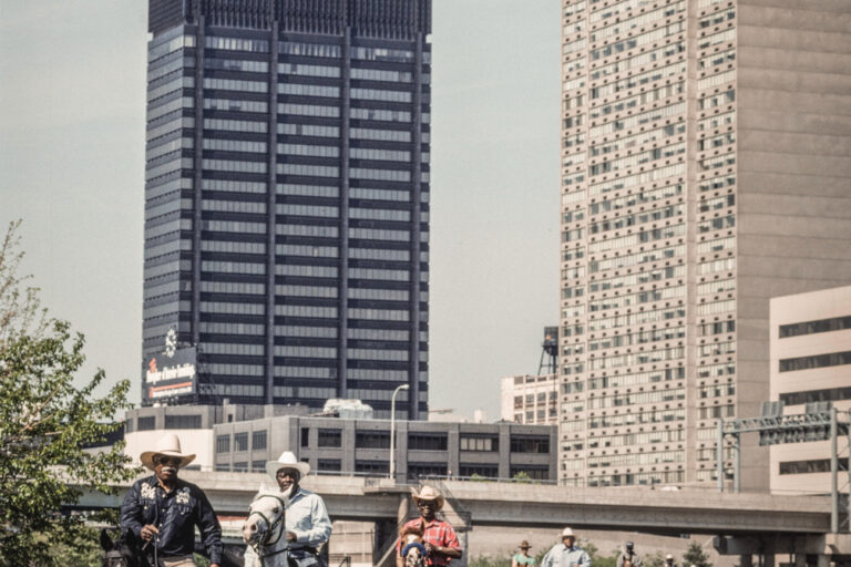 Black horse riders ride horses in Philadelphia with large buildings in the background