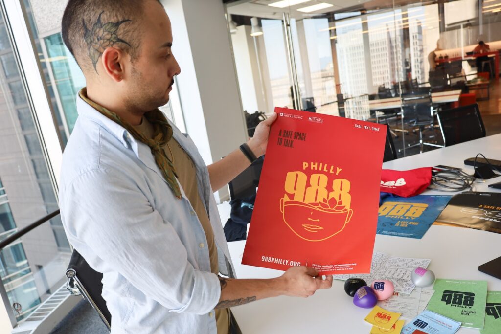 Miguel Hernandez, art director at Jeme Agency, holds up a poster about the 988 mental health crisis and suicide hotline that was designed for the School District of Philadelphia this fall, on Aug. 27, 2024