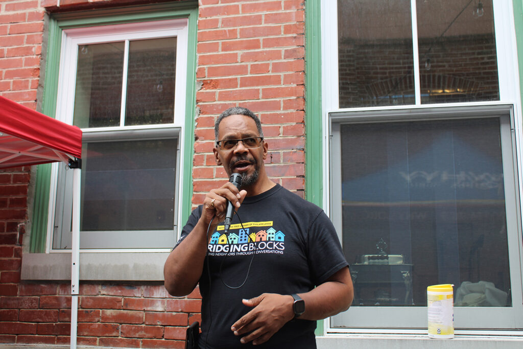 Eric Marsh, community and engagement manager at WHYY News, speaks to a crowd using a microphone at WHYY's Bridging Blocks public safety and belonging cookout Aug. 17.