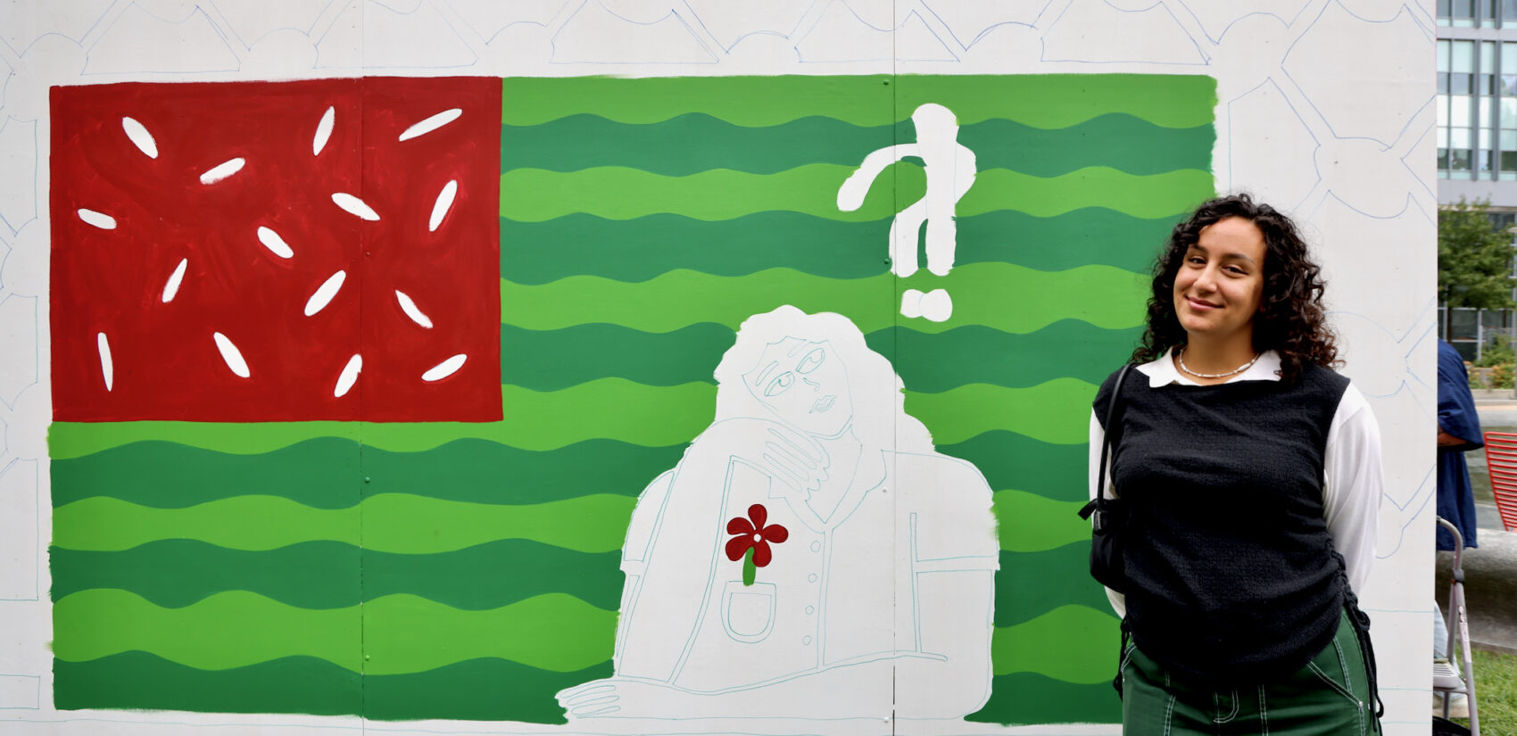 Woman stands in front of a unfinished mural of the American flag painted with watermelon colors