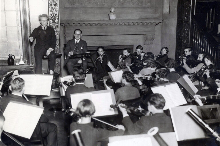 Leopold Stokowski, with help from assistant conductor Thaddeus Rich, rehearses the Curtis Orchestra