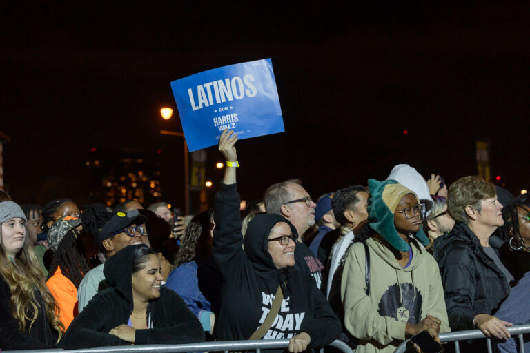 a crowd, with a woman holding a sign reading LATINOS CON HARRIS WALZ