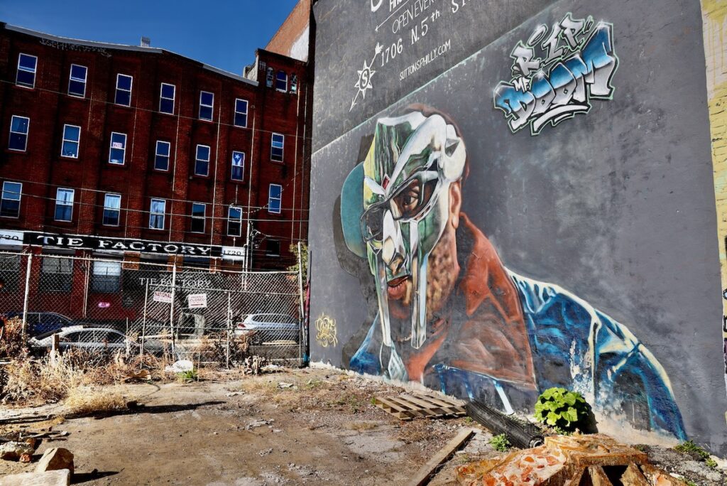 2024 11 18-e lee-philadelphia 5th and cecil b moore-mf doom mural showing tie factory A mural depicting MF DOOM