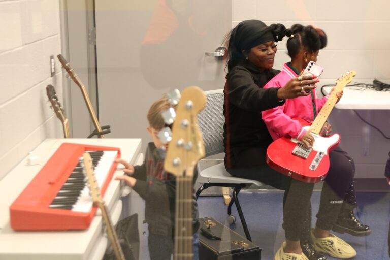 a woman sits with a child holding a guitar in a room of instruments