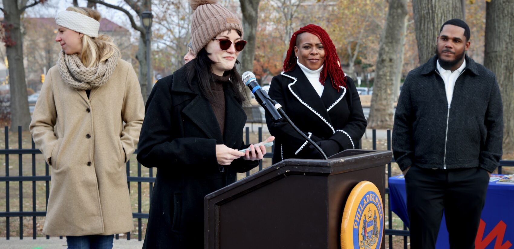 Ash Ryan speaking at a podium at a press conference