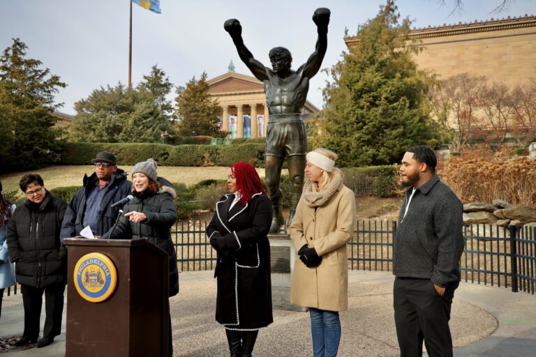 Several people standing behind a podium placed in front of the Rocky statue