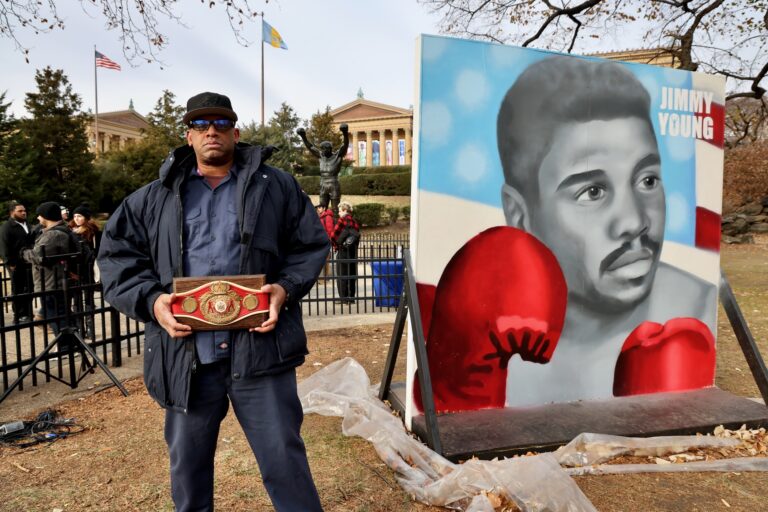 Jason Young posing in front of the large portrait of Jimmy Young with his boxing gloves