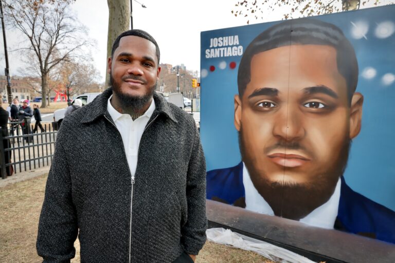 Joshua Santiago posing for a photo in front of a large portrait of him