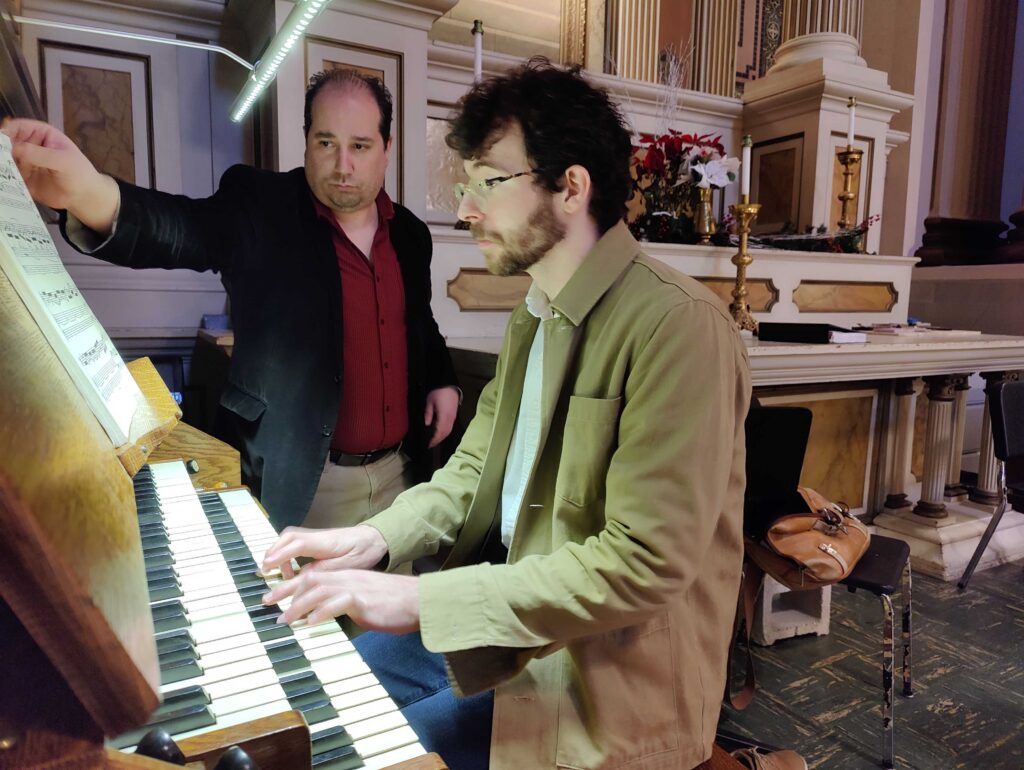 Church-of-the-Gesu-organ-2024-1 John Walhausen plays the organ in the church while Benjamin Boyle turns the pages on a music book