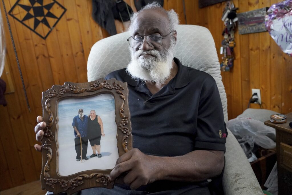 Missing Woman Sinkhole Search Kenny Pollard sitting in a chair holding up a framed photograph of him and his wife on the beach