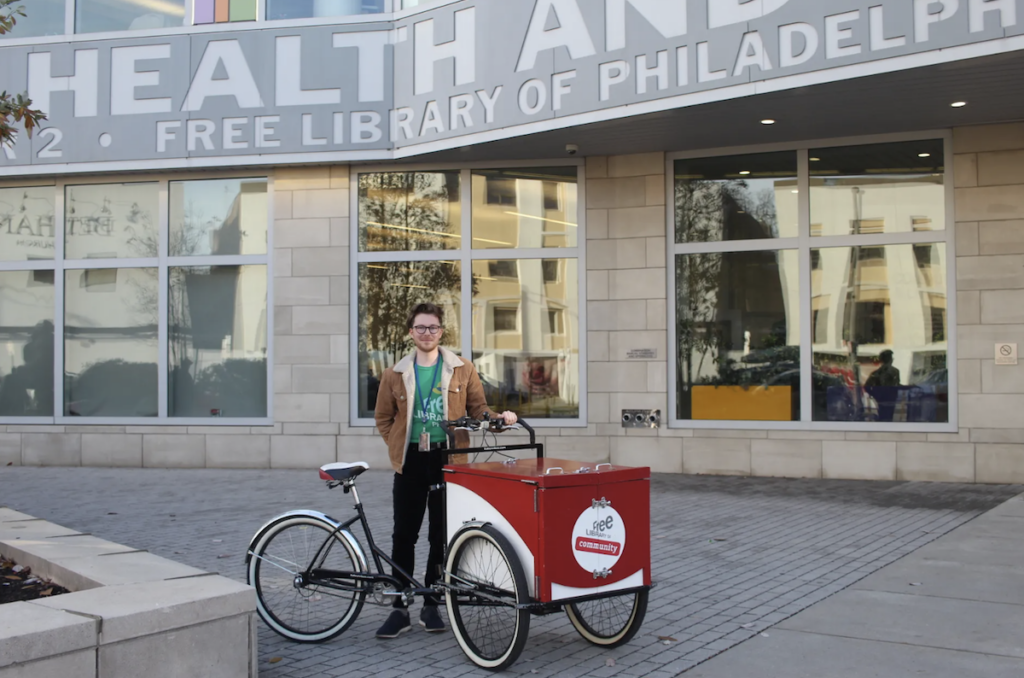 Tyler Gittelman poses for a picture with the Free Library's Book Bike outside the South Philly branch.