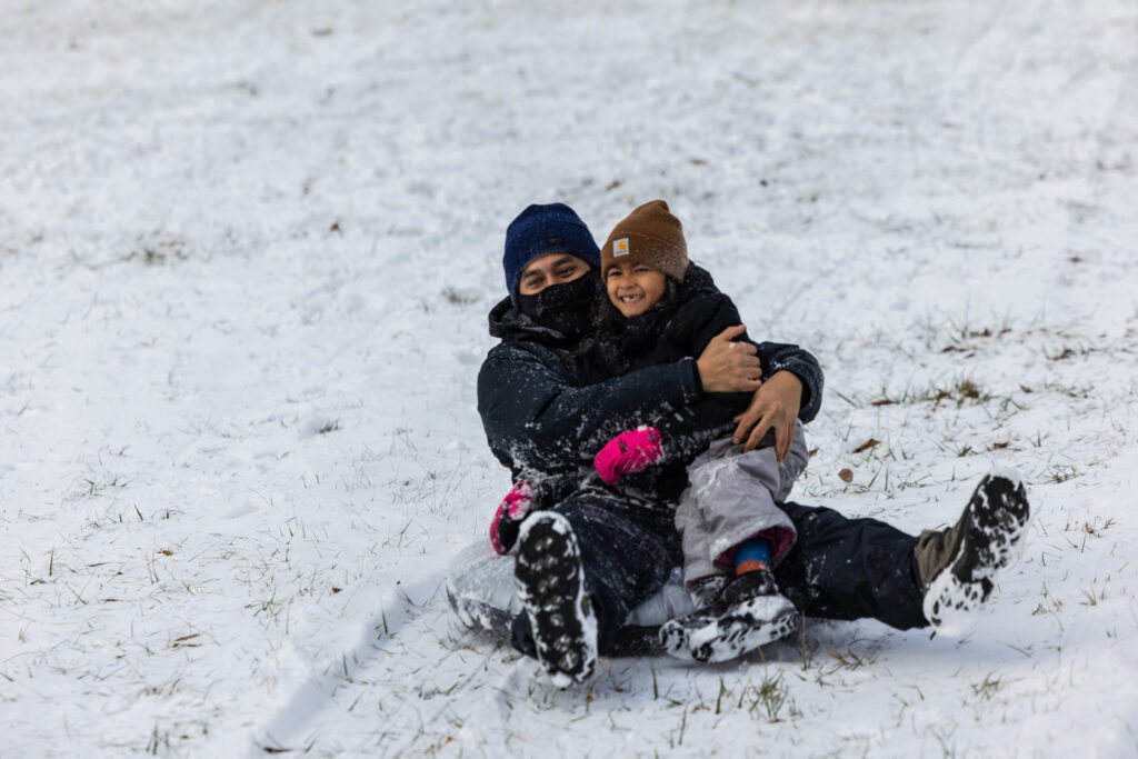 a man and child smile while sledding in the snow