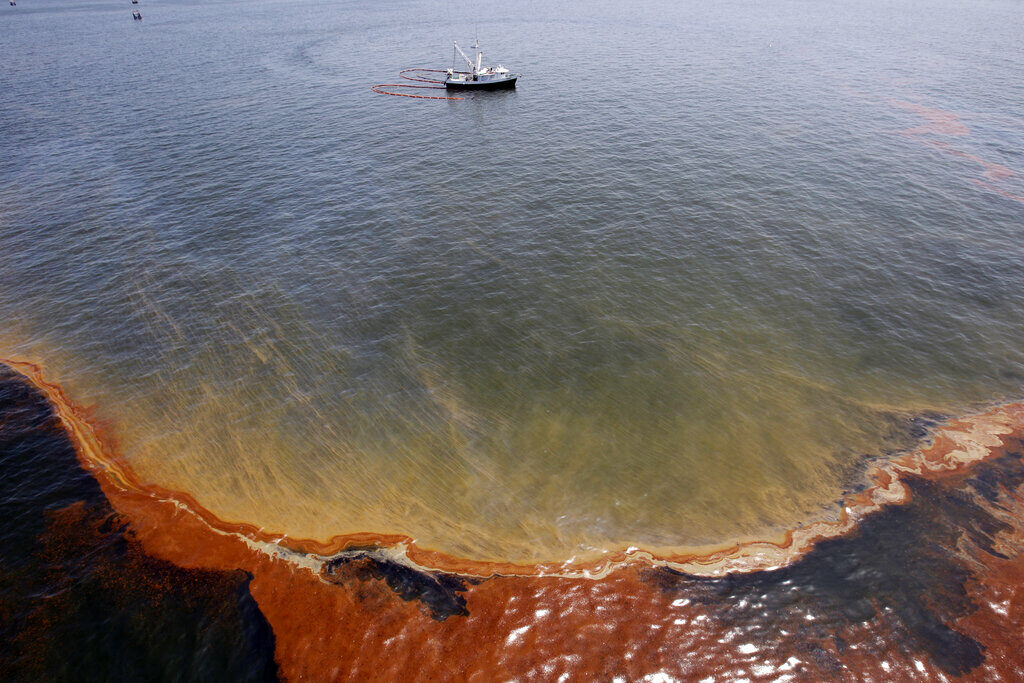 Deepwater Horizon – AP Was There FILE - This Wednesday, May 5, 2010 file picture shows a plume of oil as a shrimp boat uses booms to collect oil in the waters of Chandeleur Sound, La. On April 20, 2010, a well blew wild under a BP oil platform in the Gulf of Mexico. Eleven workers were missing that day, and would later be declared dead. Ten years after the explosion on that Deepwater Horizon rig off Louisiana's coast, The Associated Press is making the original story and photographs available. (AP Photo/Eric Gay)