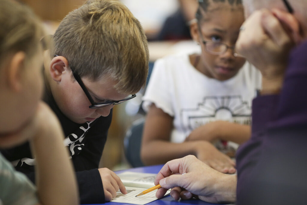 Learning to Read Student reading from a book with the help of a teacher