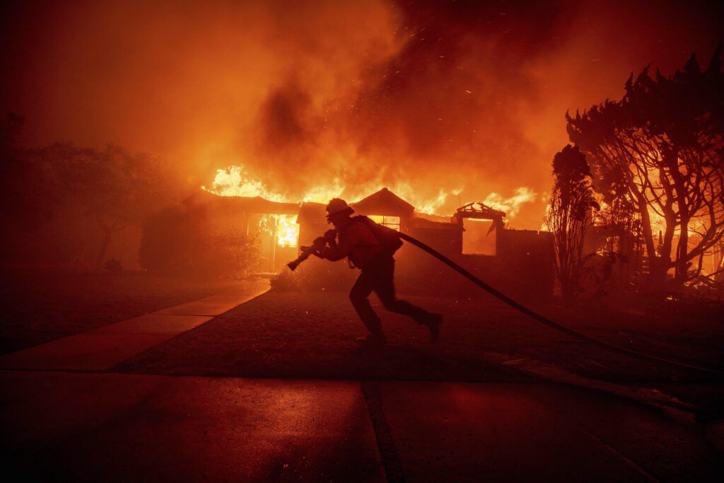 APTOPIX California Wildfires A firefighter dragging a fire hose in front of a house completely engulfed in flames