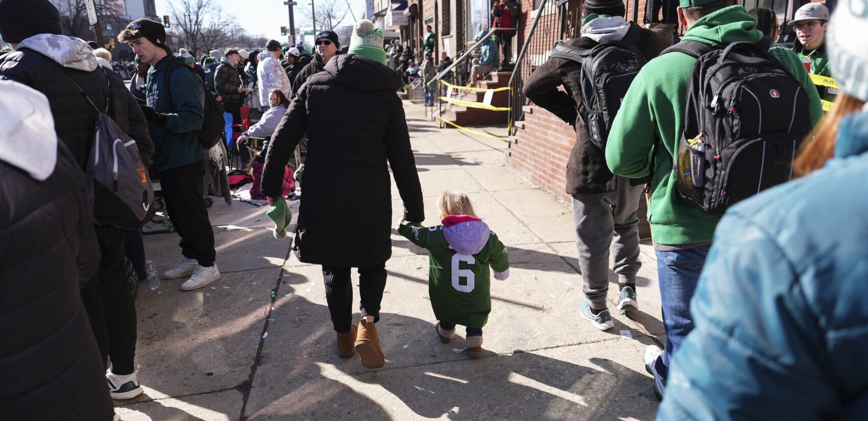 A small child walking with their parent along the parade route