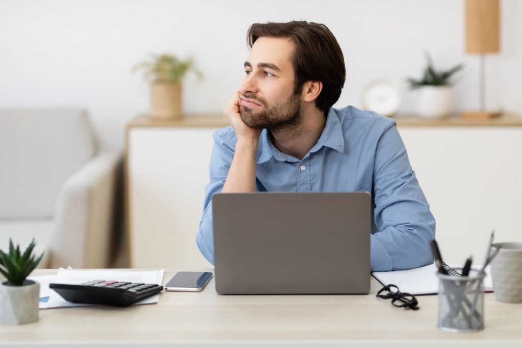 Boring Job. Bored Businessman Sitting At Laptop Computer And Looking Aside Procrastinating In Modern A bored businessman sitting at a laptop, procrastinating at work. (Photo Courtesy/Bigstock)