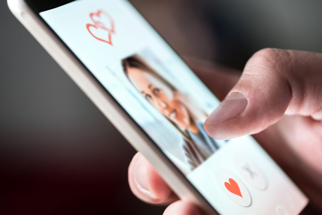 Online Dating App In Smartphone. Man Looking At Photo Of Beautiful Woman. Person Swiping And Liking A man is looking at photo of a woman on dating app. (Bigstock/TeroVesalainen)