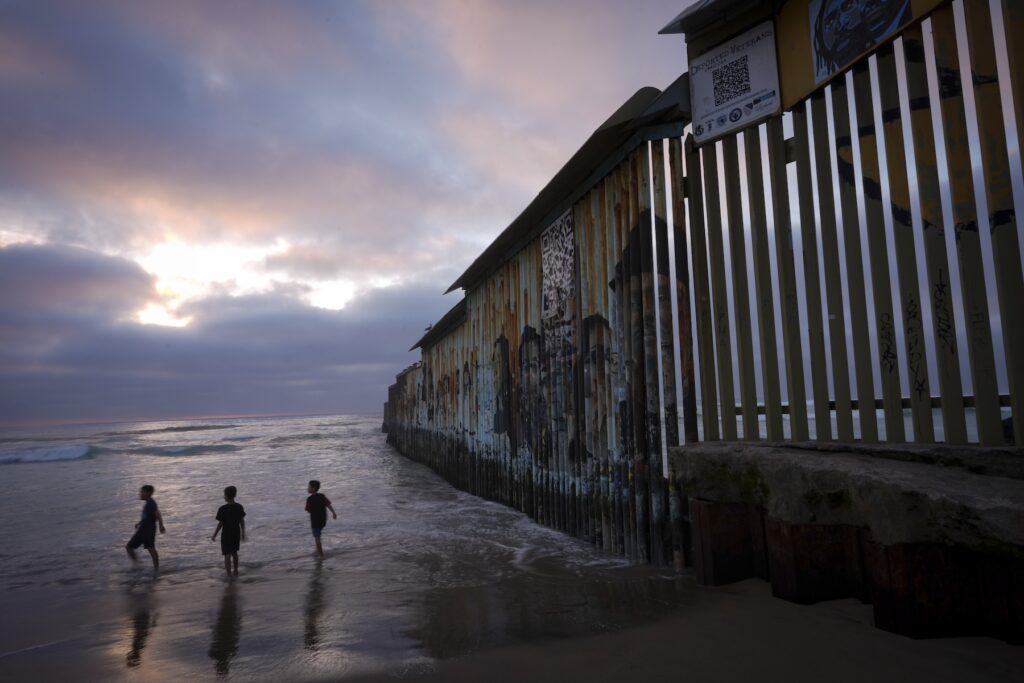 Border Immigration children playing on the beach near the border well which extends into the water