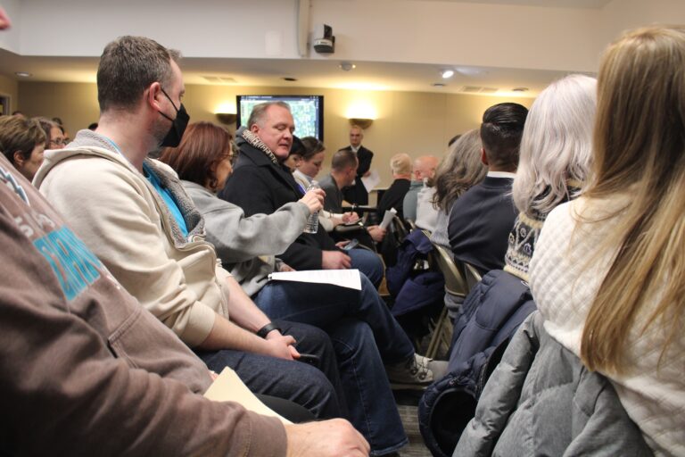 People at a town hall meeting passing a bottle of water around so they can smell it.