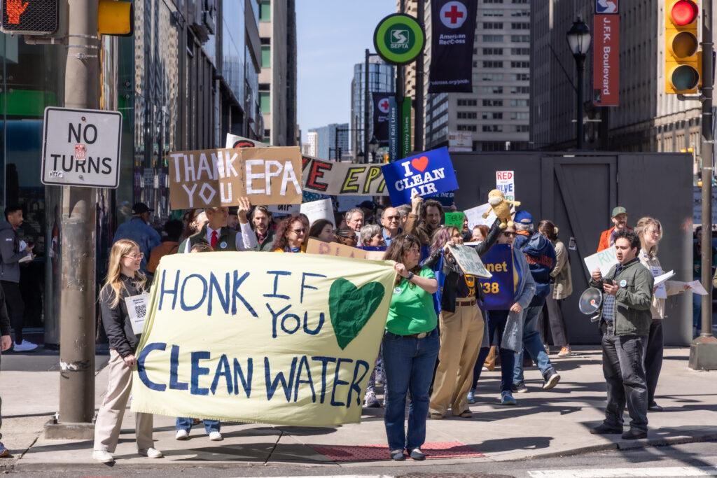 Protesters marching and carrying signs. One reads THANK YOU EPA, another reads I HEART CLEAN AIR and another reads HONK IF YOU HEART CLEAN WATER