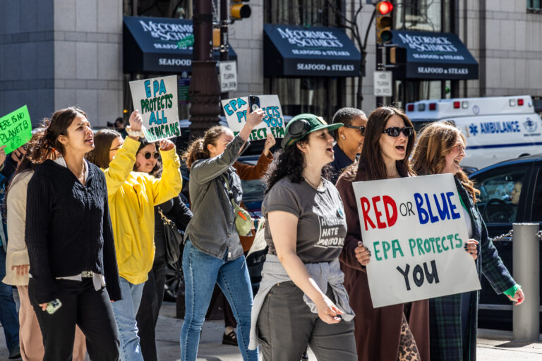 Protesters marching and carrying signs. One reads RED OR BLUE EPA PROTECTS YOU and another reads EPA PROTECTS ALL AMERICANS