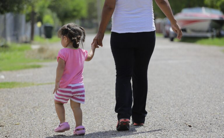 A young girl walking down the street holding onto a woman's hand